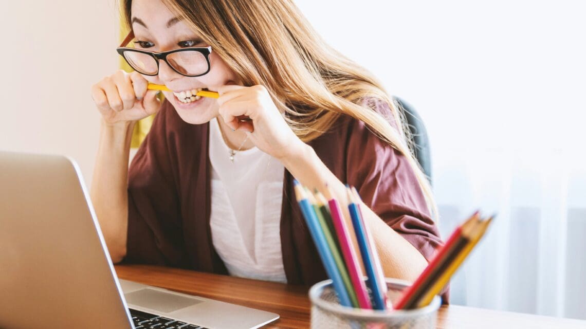 woman biting pencil while sitting on chair in front of computer